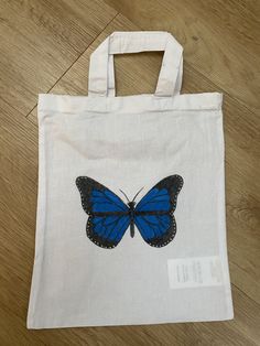 a white bag with a blue butterfly painted on the front and side, sitting on a wooden floor