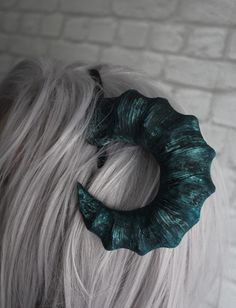 a woman with grey hair wearing a green scrunchy bun in front of a brick wall