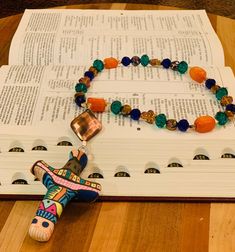 a book with a cross and beads on it sitting next to a bracelet that is laying on top of an open book