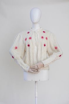 "Classic Austrian style hand knitted ivory white wool cardigan. The cardigan features a voluminous weaving embroidery. Decorated with pink floral embroidery. Buttonless, collar has a ties with a ribbon. Condition: Good vintage condition. No major flaws. Measurements: Best Fits: M-L All measurements are taken lying flat and have already been doubled. Shoulders: 44 cm /17\" Sleeves: 58 cm / 23'' Chest: 100 cm / 39\" Length: 55 cm / 21,5\"" Winter Pink Cardigan With Floral Embroidery, Winter Embroidered Cream Cardigan, Winter Cream Embroidered Cardigan, Cream Embroidered Winter Cardigan, Embroidered White Cardigan For Winter, Pink Floral Embroidered Winter Cardigan, Pink Floral Embroidery Cardigan For Winter, Embroidered Cream Cardigan For Winter, White Embroidered Knit Cardigan