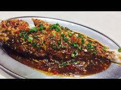 a fish covered in sauce and garnished with green onions on a silver plate