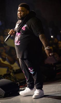 a man standing on top of a stage with a microphone in his hand and people behind him