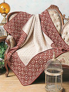 a bed covered in a red and white blanket next to a bird cage with flowers on it