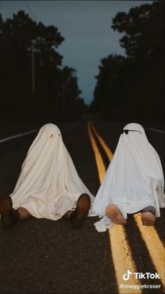 two people dressed in white sitting on the side of a road with their heads down