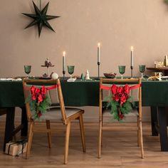 two chairs with christmas decorations on them sit at a long table in front of candles