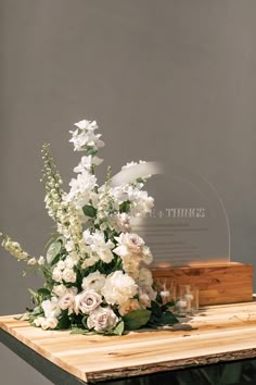 white flowers and greenery sit on a wooden table