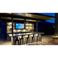 an outdoor bar with several stools and a television on the wall above it at night