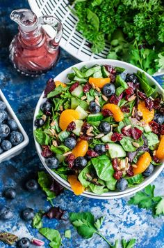 a salad in a bowl with blueberries, oranges and almonds on the side