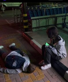 two people sitting on the ground with their cell phones up to their ear and one person laying down