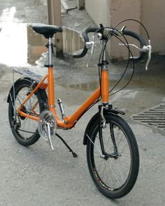 an orange bicycle parked on the side of a road in front of a building with water puddles