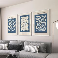 three blue and white art prints hang on the wall above a gray couch in a living room