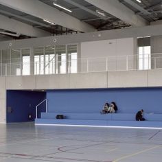 two people sitting on a bench in the middle of an indoor basketball court with blue walls