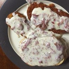 a plate topped with meat covered in gravy on top of a wooden table