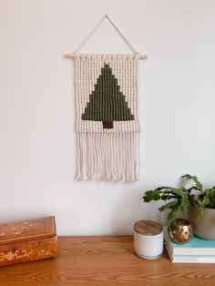 a wall hanging with a christmas tree on it next to potted plants and books