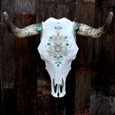 a cow skull with turquoise and white beads on it's horns hanging from a wooden fence