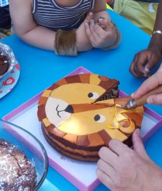 people sitting at a table cutting into a cake with a lion face on it and another person holding a knife