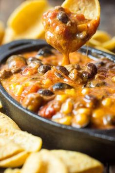 a tortilla chip being dipped with chili cheese and black beans in a cast iron skillet