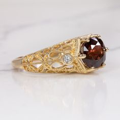 This gorgeous ring features a rich red spinel paired with a romantic, vintage style setting! The round cut spinel center has a deep and highly saturated red hue! The 14k yellow gold setting is studded with diamonds and beautifully embellished with curling filgree. The effect is classic, graceful, and sweetly feminine.The 2.56ct spinel is vibrantly saturated with very rich color. It is eye clean, luminous, and dimensional, displaying a beautiful play of light and color. The accent diamonds are br Elegant Yellow Gold Ruby Ring With Intricate Design, Gold Ruby Ring With Gemstone Accents For Anniversary, Heirloom Gold Sapphire Ring With Gemstone Accents, Formal Gold Diamond Ring With Garnet, Gold Heirloom Ruby Ring With Gemstone Accents, Heirloom Gold Ruby Ring With Gemstone Accents, Vintage Garnet Ring With Center Stone, Vintage Gold Garnet Birthstone Ring, Classic Sapphire Ring With Gemstone Accents For Wedding