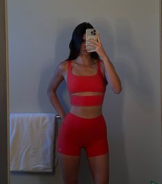 a woman is taking a selfie in her red sports bra and matching short shorts