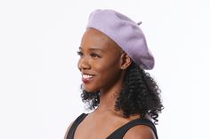 a woman with curly hair wearing a purple hat and black tank top smiling at the camera