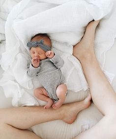 a woman holding a baby in her arms on top of a white sheet covered bed