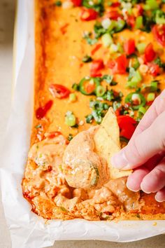 a hand dipping tortilla chips into a casserole dish filled with vegetables