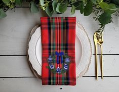 a place setting with red plaid napkins and gold cutlery on a white plate