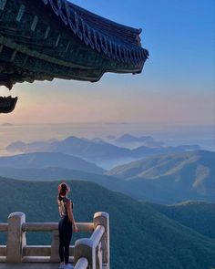 a woman standing at the top of a mountain looking out into the distance with mountains in the background