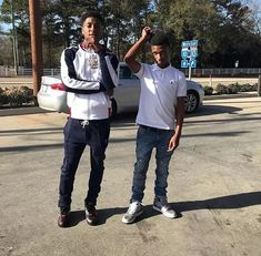 two young men standing next to each other in front of a white car on the street