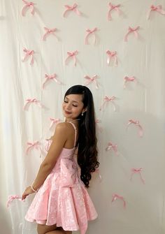 a woman standing in front of a white wall with pink bows hanging from it's sides