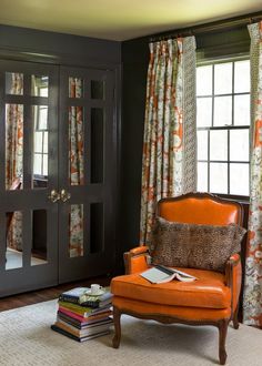 an orange chair sitting in front of a window next to a book shelf and door