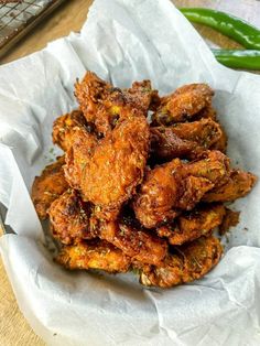 fried chicken wings in a basket on top of a table next to some green beans