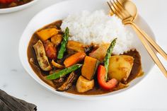 a white plate topped with rice and veggies next to a bowl of stew