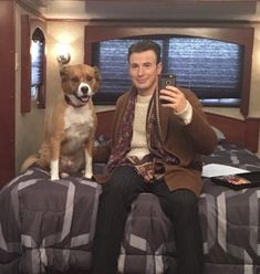 a man sitting on top of a bed next to a dog and taking a selfie