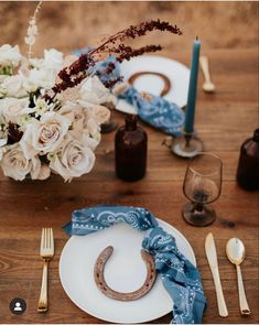 the table is set with white flowers and blue napkins, silverware, and an old - fashioned horseshoe