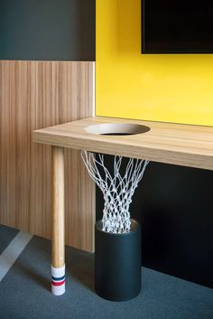 a basketball hoop in a black container next to a yellow wall with a television mounted above it