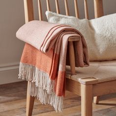 an orange and white blanket sitting on top of a wooden chair next to a pillow