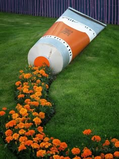 an orange and white barrel laying on top of grass next to flowers in a garden