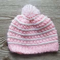 a pink and white crocheted hat sitting on top of a wooden table