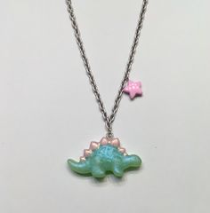 Pastel green stegosaurus necklace with glitter and pink accents on a silver chain with a pink star charm. Playful Pink Jewelry With Adjustable Chain, Green Star-shaped Handmade Jewelry, Handmade Green Star-shaped Jewelry, Playful Adjustable Silver Necklace, Green Necklace With Star Charm For Gift, Pink Star Charm Pendant Jewelry, Cute Pink Sterling Silver Necklaces, Green Nickel-free Pendant Charm Necklace, Green Sterling Silver Charm Necklace With Lobster Clasp