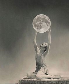 a woman sitting on the ground holding up a full moon above her head, in front of a black and white background