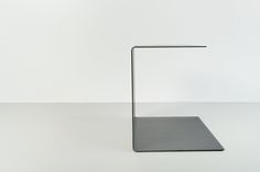 a black square object with a metal stand on the floor in front of a white wall