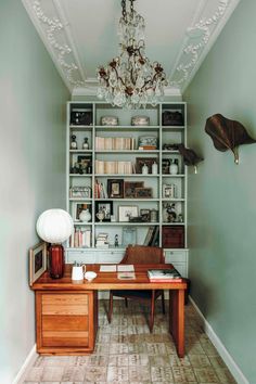 a room with a desk, bookshelf and chandelier