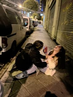 two people are sitting on the sidewalk and one person is holding a drink in his hand