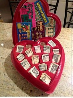 a red heart shaped box filled with lots of money sitting on top of a table