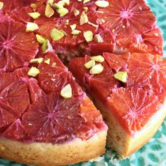 a grapefruit cake with pistachios and almonds on top sits on a green doily