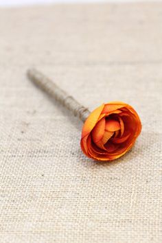 a single orange rose sitting on top of a piece of cloth next to a sewing needle