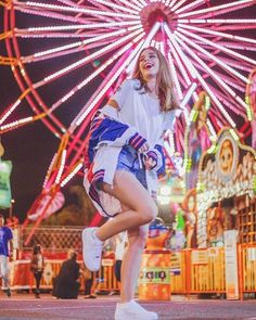 a woman standing in front of a ferris wheel with her legs spread out and wearing white sneakers