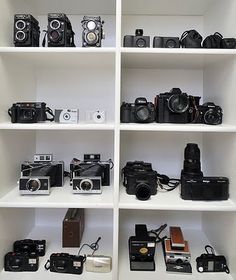 a white shelf filled with lots of different types of cameras