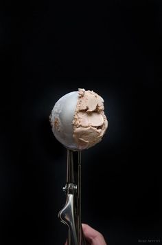 a person holding an ice cream sundae on top of a metal stand with a black background